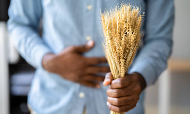 man holding stomach and bundle of grains representing celiac disease