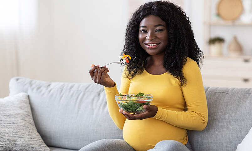 pregnant woman sitting on a sofa eating salad
